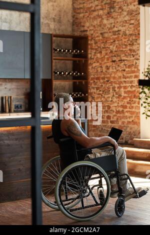 Vertikale Seitenansicht Porträt einer zeitgenössischen tätowierten Frau mit Behinderung mit Laptop während der Arbeit von zu Hause aus Stockfoto
