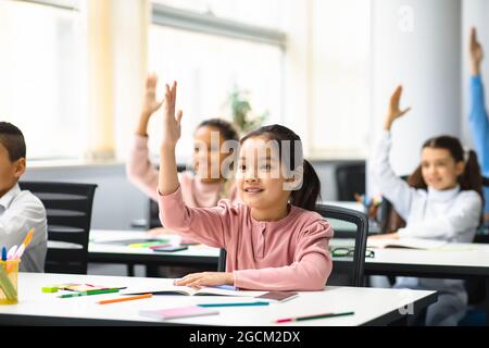 Eine vielfältige Gruppe von kleinen Schulkindern, die im Klassenzimmer die Hände heben Stockfoto