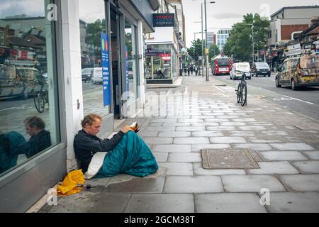 London – 2021. August: Ein Obdachloser sitzt auf dem Bürgersteig in der West Ealing High Street Stockfoto