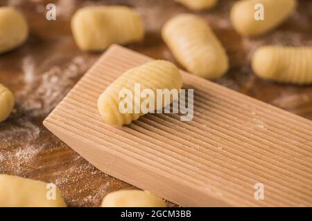 Draufsicht auf weiche rohe Teigstücke, die während der Gnocchi-Zubereitung in der Küche auf einen mit Mehl bedeckten Holztisch in der Nähe des Rippenbretts gelegt werden Stockfoto