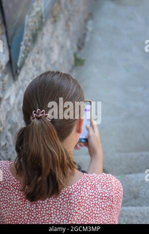 Eine junge Frau, die in der alten mediterranen Stadt auf einer Treppe sitzt und ein Mobiltelefon benutzt. Stockfoto