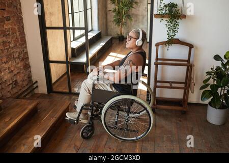 Porträt einer zeitgenössischen tätowierten Frau mit Behinderung, die Musik hört, während sie sich zu Hause entspannt und den Raum kopiert Stockfoto