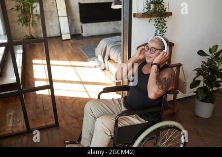 Porträt einer zeitgenössischen tätowierten Frau mit Behinderung, die Musik hört, während sie sich zu Hause entspannt, Kopierraum Stockfoto