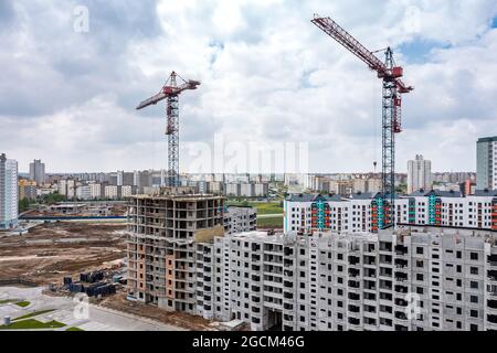 Komplex von Gebäuden im Bau und städtischen Wohngebiet von mehrstöckigen Gebäuden in der Ferne. Luftdrohne Foto. Stockfoto