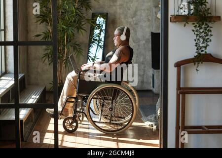 Seitenansicht Porträt einer zeitgenössischen tätowierten Frau mit Behinderung, die Musik hört, während sie sich zu Hause entspannt Stockfoto