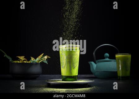 Stillleben Komposition mit traditionellem orientalischen Matcha Tee serviert in Glas Tasse mit Metall dekorativen Dekor auf Tisch mit Keramik-Schalen und frischen gree Stockfoto