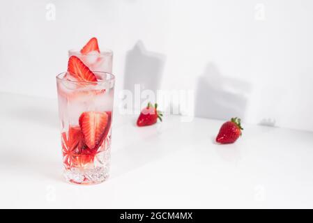 Gesundes, erfrischendes Detox-infundiertes Wasser mit frisch reifen, in Scheiben geschnittenen Erdbeeren, serviert in transparenten Gläsern vor einer weißen Wand mit Schatten Stockfoto