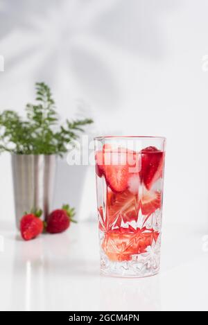 Erfrischendes Sommergetränk mit frisch geschnittenen Erdbeeren und Eiswürfeln mit Wasser, serviert im Glas auf dem weißen Tisch Stockfoto