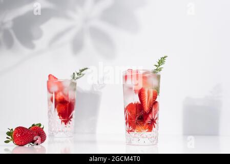 Erfrischendes Sommergetränk mit frisch geschnittenen Erdbeeren und Eiswürfeln mit Wasser, serviert in Gläsern auf weißem Tisch Stockfoto