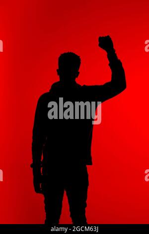 Silhouette eines nicht erkennbaren afroamerikanischen männlichen Protesters, der mit geballter Faust auf rotem Hintergrund im Studio steht Stockfoto