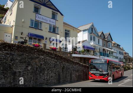 Looe, Cornwall, England, Großbritannien. 2021. Ein roter Einzeldeckerbus, der an einer Ferienunterkunft in West Looe, Großbritannien, vorbeifährt Stockfoto