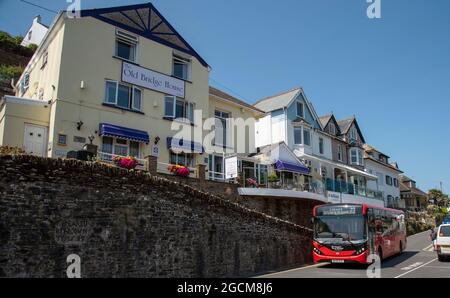 Looe, Cornwall, England, Großbritannien. 2021. Ein roter Einzeldeckerbus, der an einer Ferienunterkunft in West Looe, Großbritannien, vorbeifährt Stockfoto