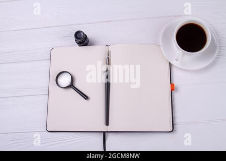 Copybook mit Glaslupe und einer Tasse Kaffee von oben. Stockfoto