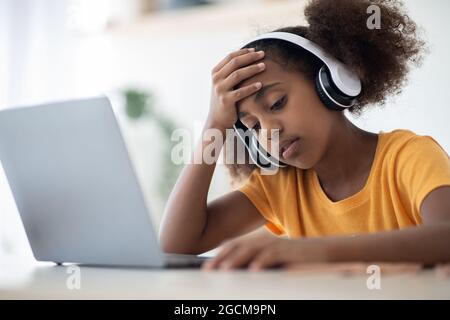 Erschöpftes schwarzes Schulmädchen, das vor dem Laptop sitzt Stockfoto