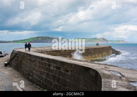 Dorset-Küste, Blick auf Menschen, die auf der Cob spazieren - die markante geschwungene Hafenmauer im Dorset-Ferienort Lyme Regis, England, Großbritannien Stockfoto