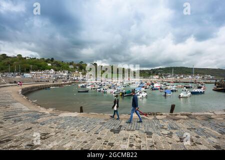 Lyme Regis, Blick auf ein Paar mittleren Alters zu Fuß auf dem Kai im Hafen von Lyme Regis, Dorset, England, Großbritannien Stockfoto