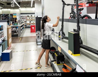 Ein Teenager-Mädchen in einem Geschäft untersucht einen Elektroroller Stockfoto