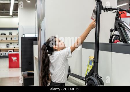 Ein Teenager-Mädchen in einem Geschäft studiert einen Anhänger auf einem Elektroroller Stockfoto