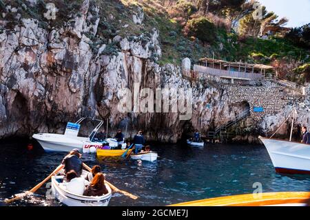 Italienische Ruderer führen Touristen durch einen schmalen Eingang zur natürlichen Meereshöhle auf Capri in die Blaue Grotte, die von den Gästen flach auf dem Rücken liegt. Stockfoto