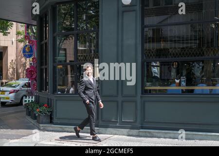 Hübscher, eleganter Mann in schwarzem Anzug, der auf der Straße in der Nähe der dunkelgrünen Wand unterwegs ist. Hochwertige Fotos Stockfoto