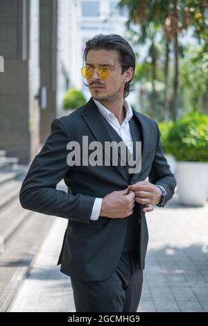 Porträt eines hübschen jungen Mannes in schwarzem Anzug und einer gelben Sonnenbrille, der zur Seite schaut. Hochwertige Fotos Stockfoto