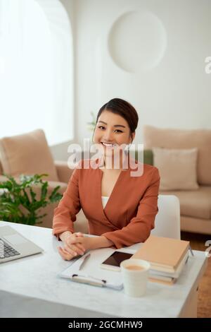 Eine hübsche Geschäftsfrau lächelt an der Kamera, während sie vor dem Computer an ihrem Schreibtisch sitzt. Stockfoto