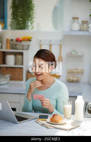 Die junge, überraschte Frau fragte sich, ob sie einen Laptop benutzte, mit einer Kreditkarte kaufte und lächelte. Stockfoto