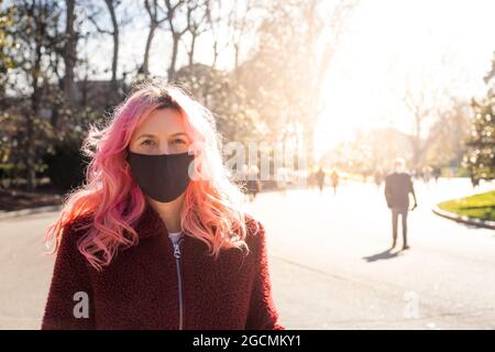 Frau mit Stoffmaske und Blick auf die Kamera in einem Park im Winter Stockfoto