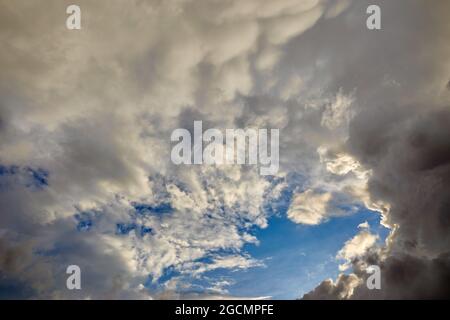 Die Sonne versteckte sich am Abend hinter den Wolken gegen den blauen Himmel Stockfoto