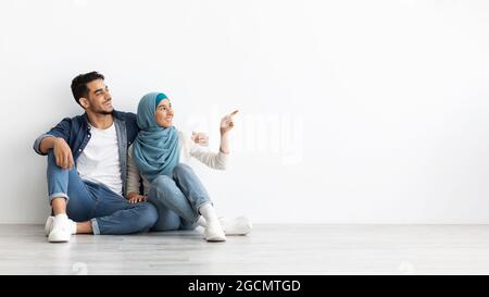 Verträumte Frau im Hijab, die mit ihrem Mann auf dem Boden sitzt Stockfoto