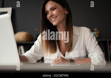 Schöne weibliche Data Analyst am Tisch arbeitet, sitzt auf einem Laptop. Stilvolle Frau in der modernen Büroumgebung. Stockfoto