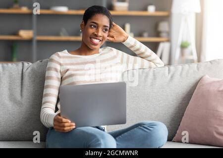 Schöne Glückliche Junge Afroamerikanische Frau, Die Zu Hause Mit Laptop-Computer Entspannt Stockfoto