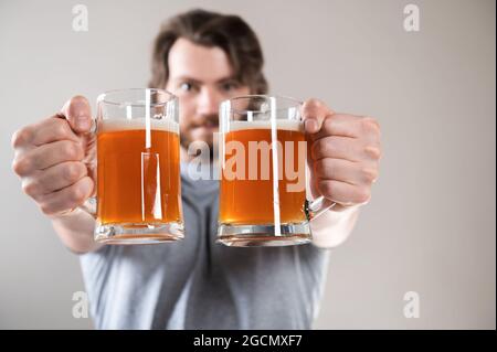 Nahaufnahme der Hand eines jungen Mannes mit zwei Tassen Bier auf hellgrauem Hintergrund Stockfoto