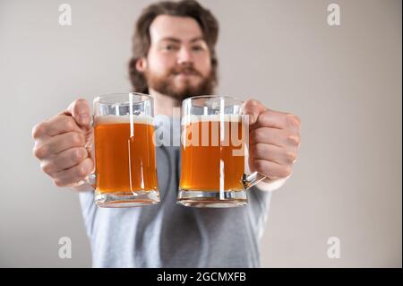 Nahaufnahme der Hand eines jungen Mannes mit zwei Tassen Bier auf hellgrauem Hintergrund Stockfoto