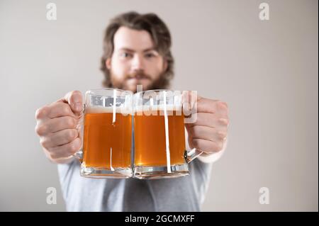 Nahaufnahme der Hand eines jungen Mannes mit zwei Tassen Bier auf hellgrauem Hintergrund Stockfoto