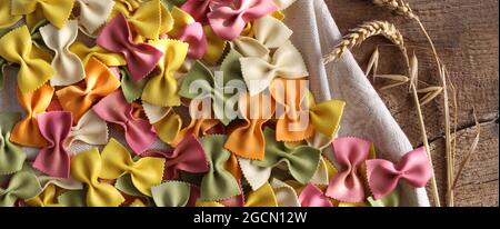 Italienische Pasta Farfalle Hintergrund mit Roggen auf alten Holz Hintergrund. Bunte Pastamuster mit Fliege. Horizontale Ebene Lay-Ansicht von oben Stockfoto