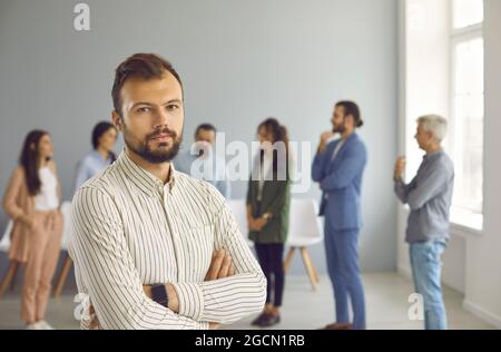 Porträt eines ernsthaften jungen professionellen Geschäftsmannes im Büro auf dem Hintergrund von Kollegen. Stockfoto