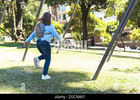 Kleines blondes Mädchen mit einem Rucksack, das in einem Park läuft Stockfoto