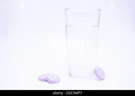 Transparentes Glas mit sauberem Wasser, daneben löslich. rosa Tabletten Vitamin C, Nahrungsergänzungsmittel, Schmerzmittel sofort oder auflösen. Stockfoto