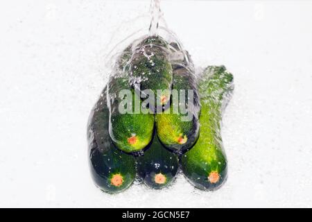 Zucchini liegen auf einer weißen Oberfläche. Zucchini mit Spritzwasser werden in einem Haufen auf einer weißen Oberfläche gestapelt Stockfoto