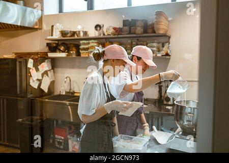 Mitarbeiter geben Milch in eine Schüssel und machen Teig mit Kollegen in der Craft Bakery Stockfoto