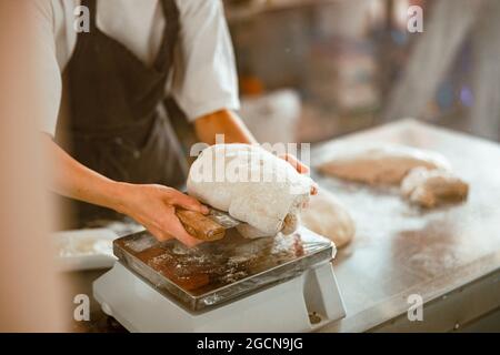 Frau schneidet in einer modernen handwerklichen Bäckerei Stück frischen rohen Teig Stockfoto