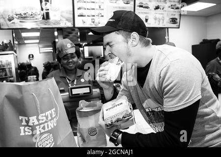 PRETORIA, SÜDAFRIKA - 06. Jan 2021: Eine Graustufe eines Mannes, der aufgeregt einen Burger in einem neu eröffneten Burger King Restaurant isst Stockfoto