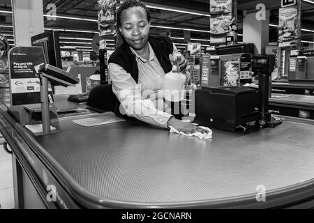 KAPSTADT, SÜDAFRIKA - 06. Jan 2021: Ein Kassenpersonal an der Kasse wischte während eines Virenausbruchs Oberflächen im Pick 'n Pay-Lebensmittelgeschäft ab Stockfoto