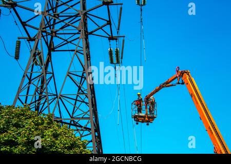 Dnepropetrovsk, Ukraine - 08.06.2021: Hochspannungs-Hochspannungsübertragung Tower Arbeiter mit Kran und blauen Himmel. Hydro-Linemen an Auslegerliften arbeiten Stockfoto