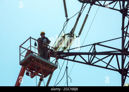 Dnepropetrovsk, Ukraine - 08.06.2021: Hochspannungs-Hochspannungsübertragung Tower Arbeiter mit Kran und blauen Himmel. Hydro-Linemen an Auslegerliften arbeiten Stockfoto