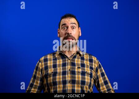 Junger Mann mit einer verängstigten Pose auf blauem monochromen Hintergrund Stockfoto