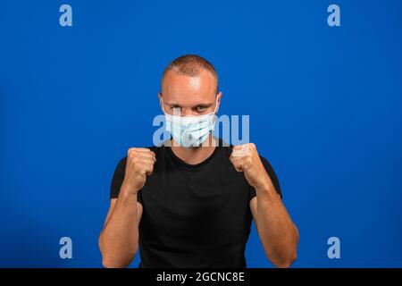 Portrait des wütenden Mannes mit chirurgischer medizinischer Maske in schwarzem Casual Style Shirt mit Boxfäusten und Blick auf die Kamera und bereit zum Angriff. Indoor Stockfoto