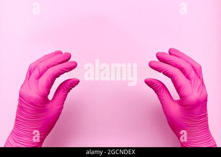 Medizinischer Spatel horizontal in zwei Händen in Schutzhandschuhen. In rosa Tönen. Stockfoto
