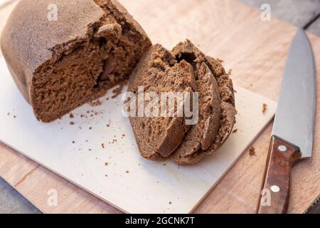 Frisch gebackenes, braunes Borodino-Brötchen, in Scheiben geschnitten, neben einem großen Messer. Frische hausgemachte Backwaren. Selektiver Fokus. Stockfoto